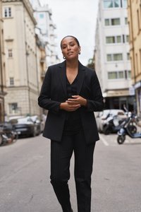 Svart randig kostym med en figurnära kavaj och matchande byxor, i kombination med en svart väst. Silverfärgade hoopörhängen fulländar looken. Urban bakgrund.