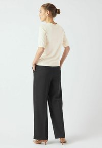 Top in maglia a maniche corte di colore crema abbinato a pantaloni neri a vita alta. I pantaloni presentano tasche laterali e un design a gamba dritta.