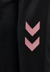 Svarta träningsbyxor med en slät textur, som har ett rosa prickigt chevronmönster på sidan.