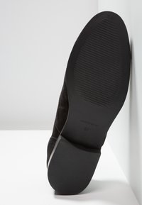 Chaussure en daim noir avec une semelle en caoutchouc, présentant une surface texturée, un talon anglé et un détail embouti "Fabriqué en Espagne". Taille 37.