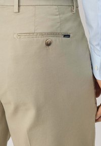 Khaki pants with a smooth texture, featuring a back pocket secured with a button and a brand label. The fabric appears sturdy and well-stitched.