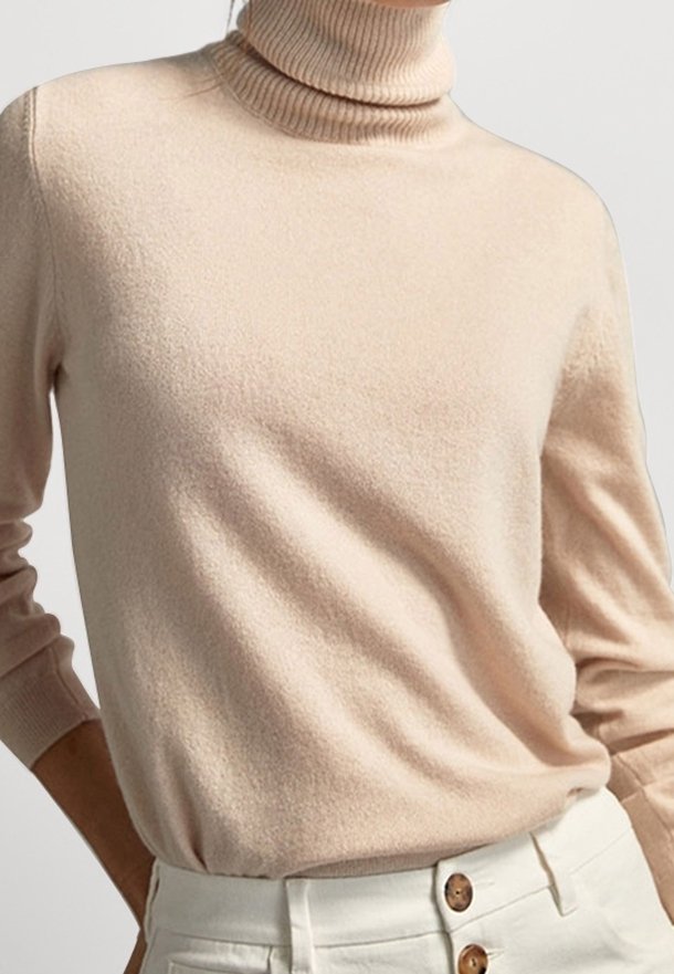 Pull à col roulé beige à manches longues associé à un pantalon blanc taille haute avec de gros boutons marron.