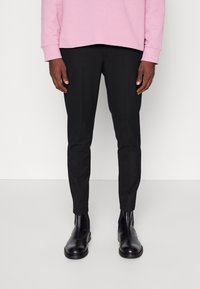 Pantaloni neri su misura a vestibilità slim, con una consistenza liscia e senza motivi visibili, abbinati a stivaletti neri alla caviglia. Felpa rosa sopra.