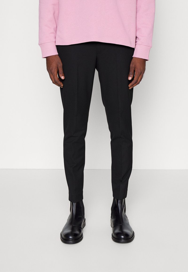 Pantaloni neri su misura a vestibilità slim, con una consistenza liscia e senza motivi visibili, abbinati a stivaletti neri alla caviglia. Felpa rosa sopra.
