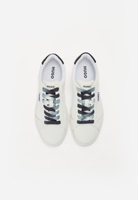 Baskets en toile blanches avec le logo HUGO, lacets bleu marine et bleu clair, bout rond et semelle texturée. Accents noirs au talon.