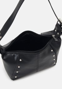 Sac d'épaule en cuir noir avec des clous en argent, fermeture éclair supérieure partiellement ouverte, bandoulière unique et compartiment interne visible.