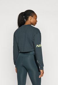 Afklippet mørkegrå sweatshirts med lange ærmer og Nike-logo i neongul på venstre arm, parret med højtaljede teal leggings.