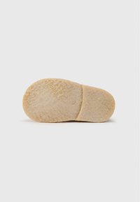 Semelle en caoutchouc avec une surface texturée beige. Présente un bout arrondi et une couture centrale pour plus de flexibilité. Design épuré et minimal.