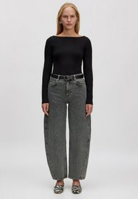 Schwarzer, langärmliger Bodysuit, hoch taillierte graue weite Jeans, schwarzer Gürtel mit silberner Schnalle, Ballerinas mit Zebra-Muster, glattes Haar, große Ohrringe.