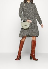 Abito floreale nero con maniche lunghe, gonna ampia; stivali marroni al ginocchio con punta quadrata; borsa a tracolla verde con chiusura a patta.