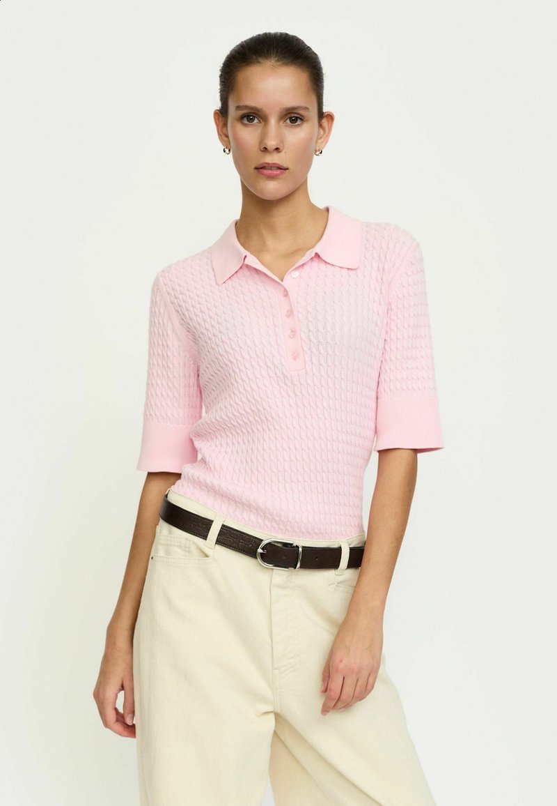 Polo tričko svetloružovej farby z textúrovanej pleteniny s krátkymi rukávmi a špicatým golierom, s gombíkovým zapínaním, kombinované s krémovými nohavicami.