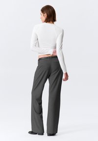 Haut blanc à manches longues associé à un pantalon gris à jambes larges. Le pantalon présente une texture lisse et des passants pour ceinture. Le dos du haut est ajusté.