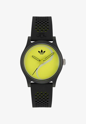 Must mustraht, millel on tekstuurne rihm; ümmargune kollane kellaplaad, millel on keeris- ja mustad näpud, ning ülaosas Adidas'i logo.