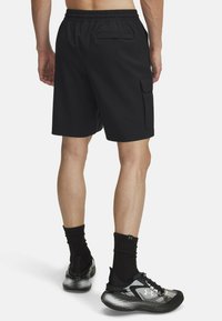 Pantalones cortos de carga negros con cinturilla elástica, dos bolsillos laterales y un bolsillo trasero. Tejido suave con un corte relajado, combinados con zapatillas deportivas negras.