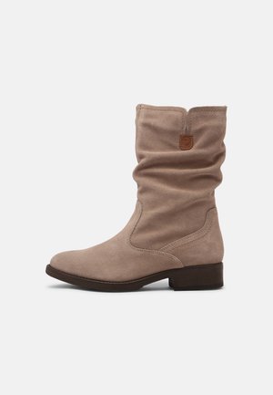 Beige ruskindsstøvle til midt på læggen med løs skaft, rundet tå, lav stablet hæl og en lille brun træktab øverst.