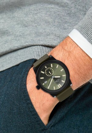 Schwarze Armbanduhr mit rundem Ziffernblatt, grünem Ziffernblatt und lumineszenten Stundenmarkierungen. Verfügt über ein olivgrünes Silikonarmband und eine Datumsanzeige.