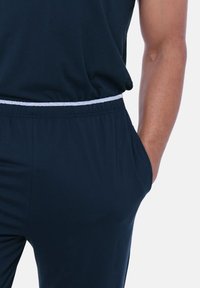 Navyblåt træningssæt med afslappet pasform, der har elastisk talje med hvid snøre og sidelommer. Blød, glat stoftekstur.