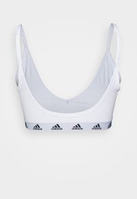 Bela športna braletka z nastavljivimi naramnicami, rebrastim elastičnim trakom, ki vsebuje črne Adidasove logotipe, in gladkim, lahkim materialom.