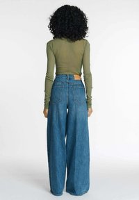 Olijfgroene lange mouwen top in combinatie met een hoge taille, wijde jeans van blauw denim. Heeft gestikte zakken en een gestructureerde afwerking.