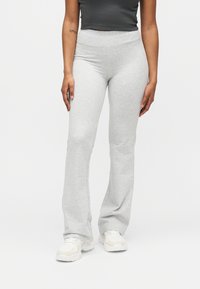 Personne portant un pantalon de survêtement taille haute gris clair, des baskets blanches et un top court gris foncé sur un fond blanc.