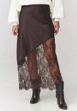 Brązowa satynowa spódnica z asymetrycznym dołem, ozdobiona przezroczystą koronką z kwiatowymi wzorami na dolnej krawędzi. Czarne botki za kostkę dopełniają całość.
