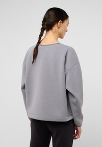 Felpa grigia con scollo a girocollo, maniche raglan e una texture liscia. Presenta una vestibilità rilassata e un orlo a costine.