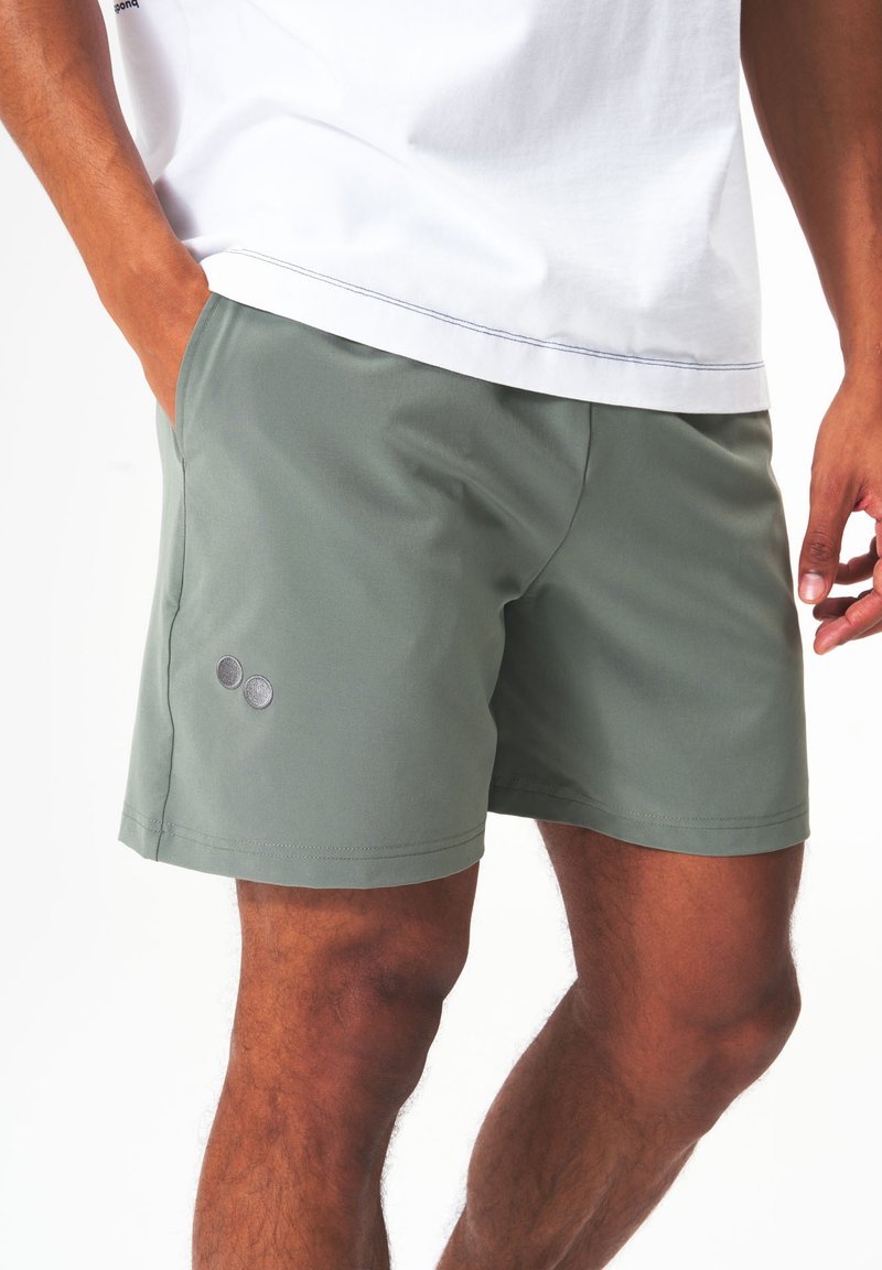 Grüne Shorts aus glattem Stoff mit klassischer Passform, zwei runden Logopunkten und sauberer Naht entlang des Saums.