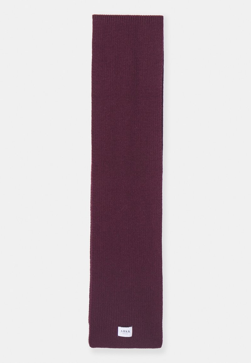 Longue écharpe tricotée en violet foncé avec une petite étiquette blanche rectangulaire près d’une extrémité portant la mention ARKK.