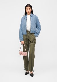 Τζιν μπουφάν σε ανοιχτό μπλε, λευκό πουκάμισο, παντελόνια ελιάς πράσινου, μικρή ροζ τσάντα χειρός και μαύρα παπούτσια με μυτερό άκρο. Χαλαρή εφαρμογή και καθημερινό στυλ.