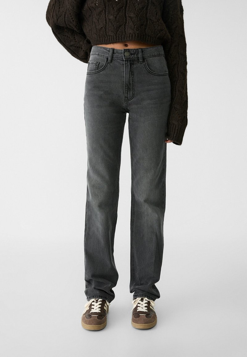 Jeans grises con un corte recto, que presentan un diseño estándar de cinco bolsillos y ligeras decoloraciones. Combinados con zapatillas marrones y blancas.