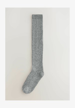 Graue knielange Socke mit gerippter Struktur, ausgestattet mit einer verstärkten Zehen- und Bündchenpartie. Hergestellt aus einem weichen, dehnbaren Material für hohen Tragekomfort.