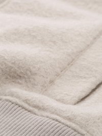 Beige textured fabric close-up showing a soft, fluffy material with a ribbed knit edge, highlighting texture and stitching details.