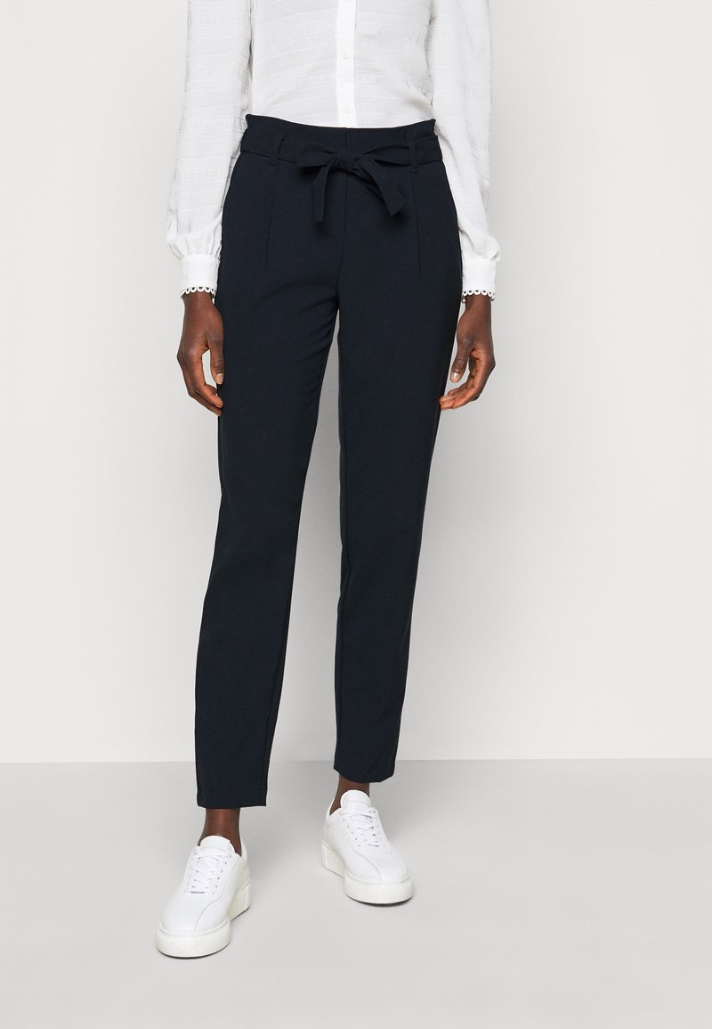 Marinblå byxor med bälte i midjan, tapered ben och sidfickor. Kombineras med vita snörade sneakers. Slät tygkvalitet och skräddarsydd passform.