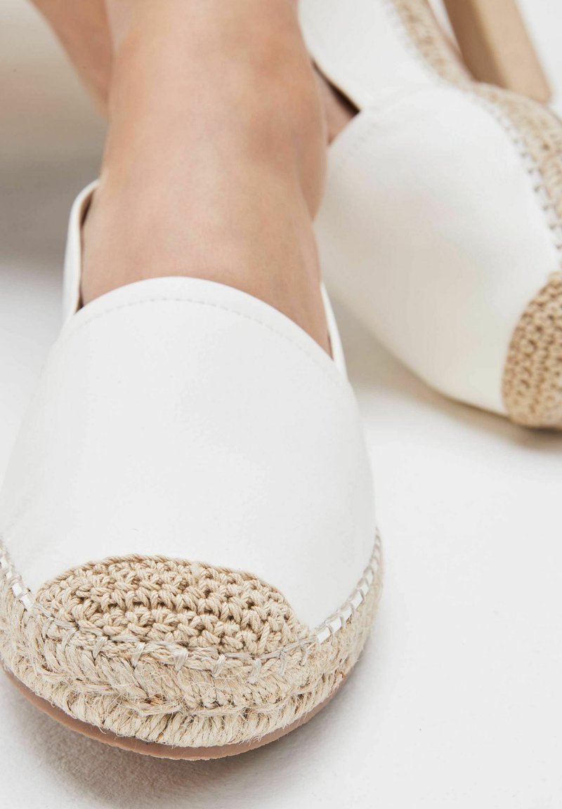 Valkoinen espadrille, jossa on kudottu beige varvaskorkki. Yläosa on sileää nahkaa, ja siinä on juuttinarusta valmistettu pohja, jossa on näkyvää tikkausta reunoilla.