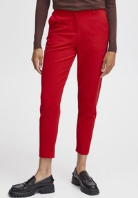 Červené přizpůsobené kalhoty mají slim fit, boční kapsy a přední záhyby. Kombinují se s černými silnými loafery pro kontrast.