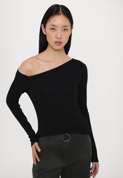 Zwarte geribde langemouwe top met een asymmetrische halslijn, een gladde textuur en een getailleerde pasvorm, gecombineerd met donker groene broek en een riem.