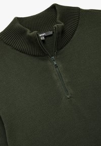 Dunkelgrüner Strickpullover mit hohem Rippenkragen und Reißverschluss, aus strukturiertem Stoff und in entspannter Passform.