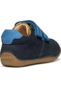 Scarpa in pelle blu e blu navy con fascia in Velcro, forma arrotondata, suola in gomma e logo Geox sul retro. Presenta dettagli cuciti.