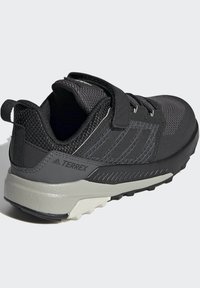 Zapatos exteriores negros con parte superior de malla y sintético, correa ajustable, tejido texturizado y suela rugosa para tracción.
