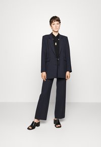 Navyblazer med två framfickor, tillsammans med en figurnära svart topp med utskärning, och vida navybyxor. Svarta klacksandaler.