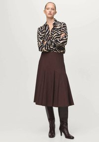 Rjavé nabrano krilo v kombinaciji s črno in bež bluzo z zebra vzorcem. Model nosi bordo škornje do kolen. Po celotni površini gladka tekstura tkanine.