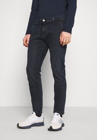Mörkblå denimjeans med slim fit, som har fem fickor och knäppning fram, vilka bärs med vita och grå sneakers.