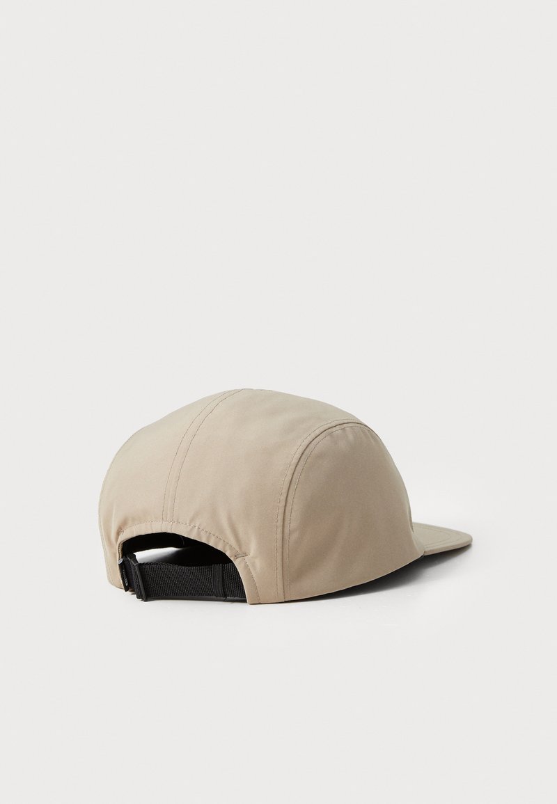 Beige pet met een gebogen klep, van zacht materiaal en een verstelbare zwarte band aan de achterkant. Heeft subtiele stikdetails.