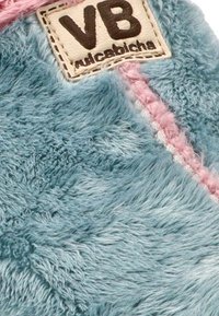 Tejido de felpa azul suave con un acento rosa. Presenta una etiqueta cosida con "VB" y una superficie texturizada.
