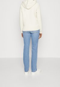 Sweat-shirt à capuche crème associé à un jean droit bleu clair et des baskets blanches, arborant un design simple et épuré avec un matériel minimal.