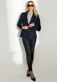 Marineblazer mit taillierter Passform, kombiniert mit schwarzen schmalen Hosen. Strukturierte gestreifte Bluse, ergänzt durch elegante schwarze spitze Absätze.
