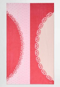 Rechthoekige strandhanddoek met een roze en rode kleurenschema, bedekt met stip- en geometrische patronen, en witte tekst en logo-accenten. Zachte textuur.