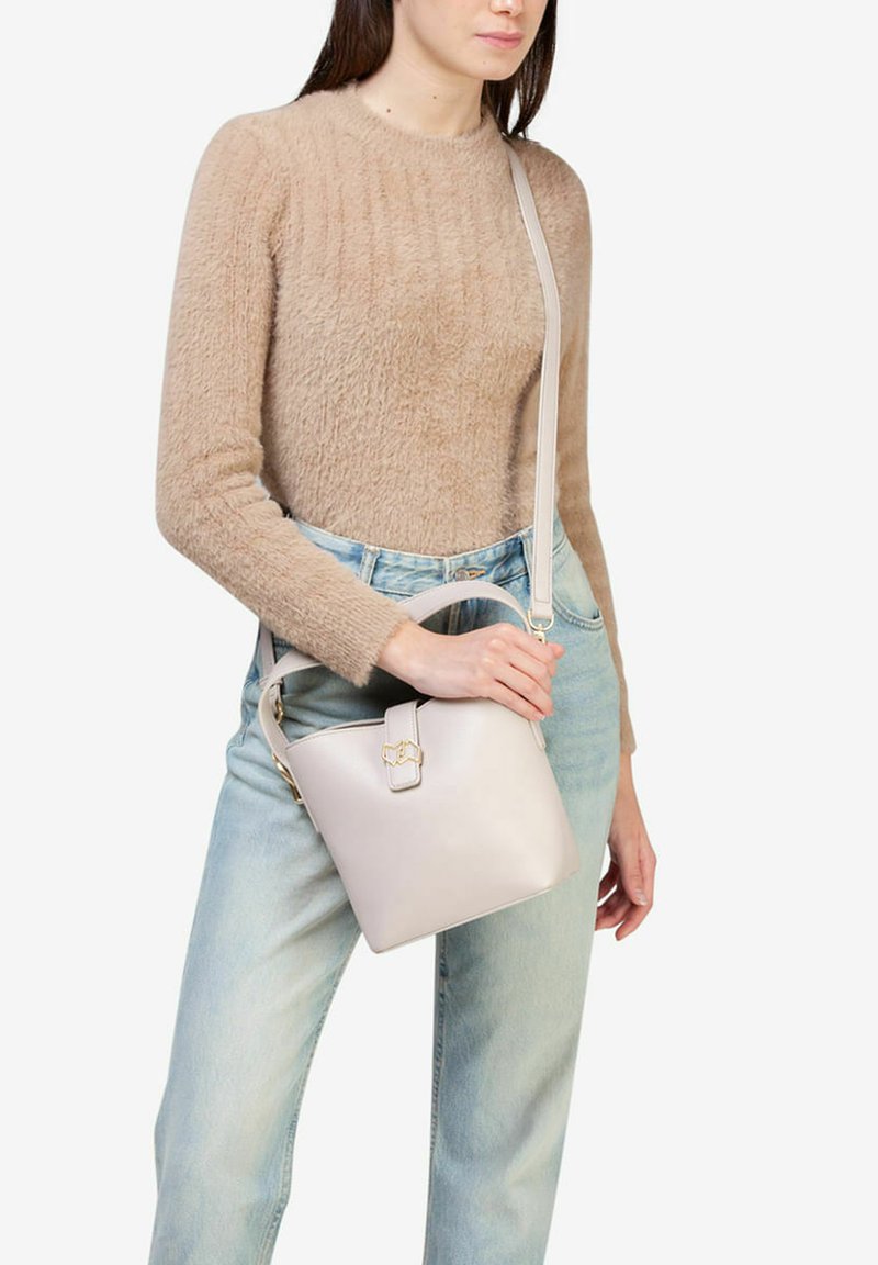 Lys grå læder bucket bag med en topklap, gyldent hardware og en aftagelig rem. Båret med lys denim og en tekstureret beige sweater.