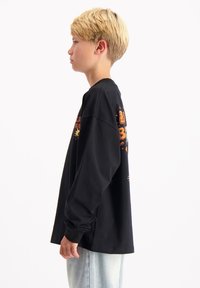 Zwart T-shirt met lange mouwen en grafische prints in oranje en geel. Heeft een losse pasvorm en een ronde hals, gestyled met een lichte spijkerbroek.