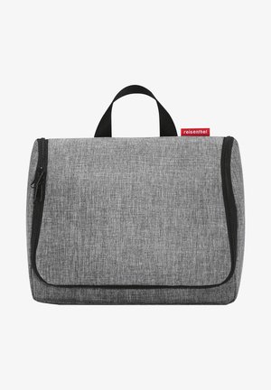 Grau gefärbtes Kosmetiktäschchen aus Stoff mit strukturiertem Finish, schwarzem Reißverschluss und einem oberen Griff. Mit einem roten Etikett, auf dem der Markenname steht.